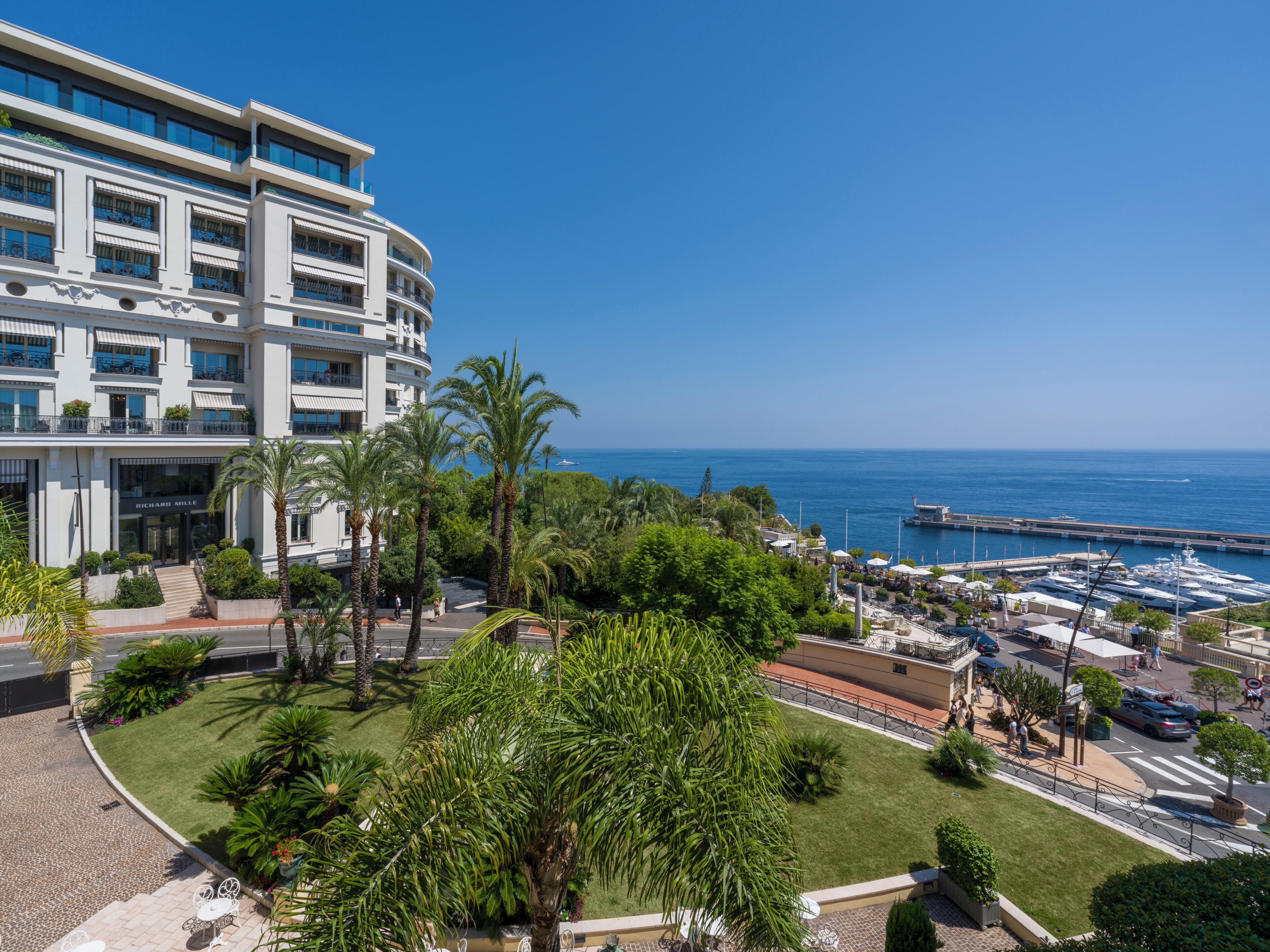 Un hôtel avec vue sur la mer, les palmiers et un port de plaisance.