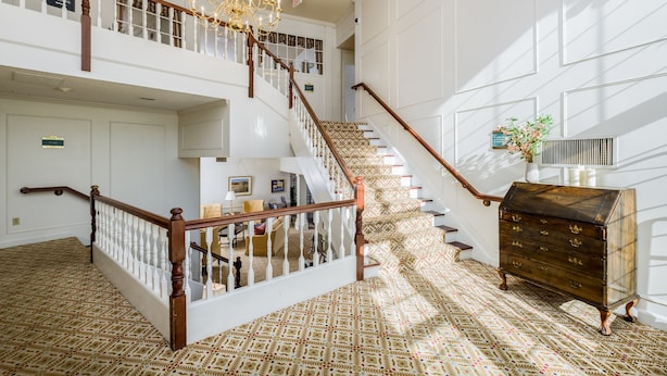 Un hall d’entrée spacieux, agrémenté d’un magnifique escalier, d’un lustre et d’un tapis à motifs.