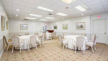 A conference room with multiple tables and chairs, white walls, framed pictures, and an exit sign.