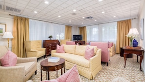 Un salon bien éclairé, avec un canapé à motifs, des fauteuils, un téléviseur et une moquette à motifs.