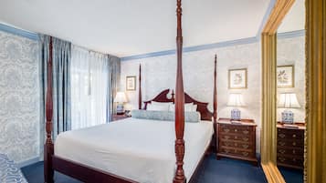 Una cama con dosel en una habitación de hotel, con un espejo grande, dos mesitas de noche con lámparas y papel tapiz estampado.