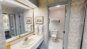 Un bany amb un mirall gran, un lavabo, un vàter i una zona de dutxa.