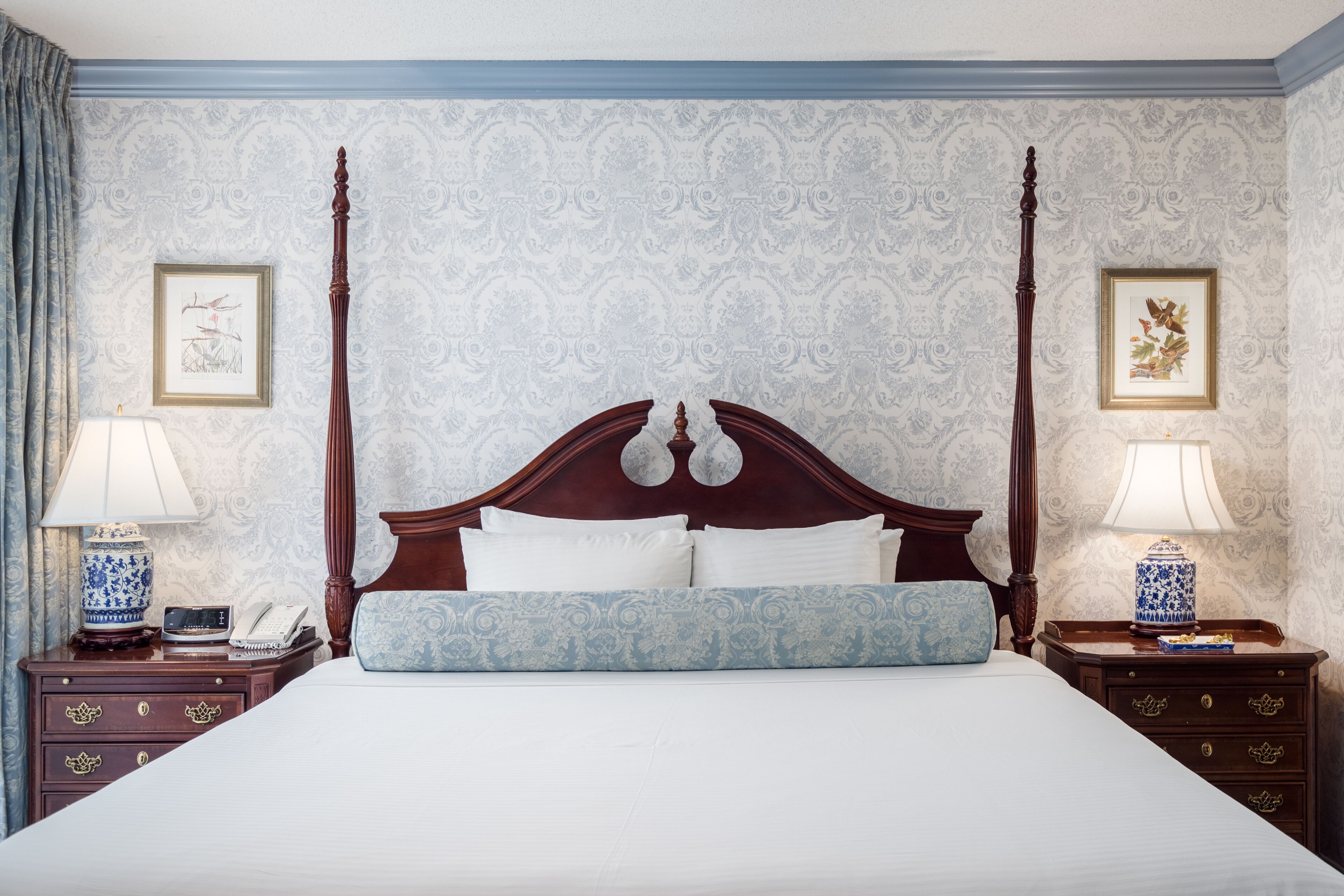 A four-poster bed with a wooden headboard, two bedside tables with lamps, and a patterned wallpaper.