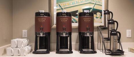 Three coffee makers labeled "HEARTH ROOM" on a counter with white mugs and a coffee pot.