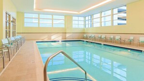 Una piscina interior con agua cristalina, rodeada de sillones de descanso y un suelo de baldosas.
