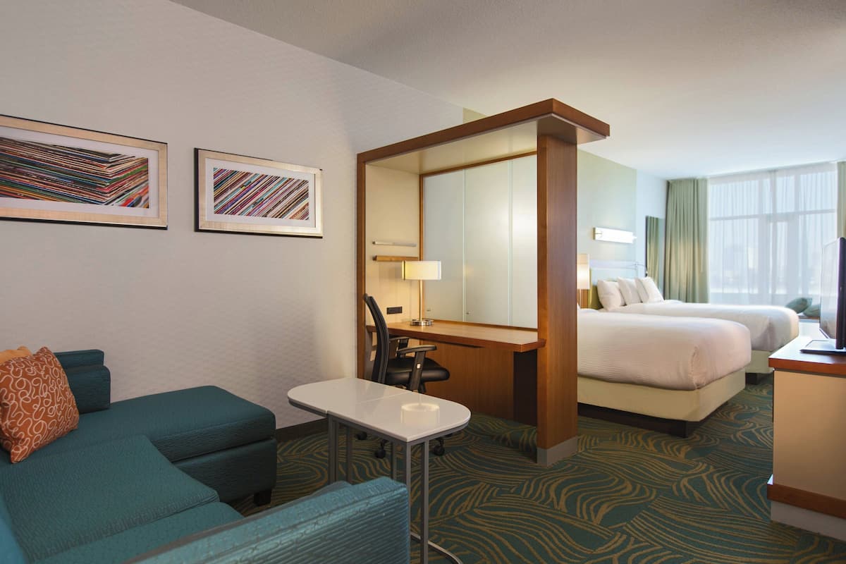 Ein Hotelzimmer mit einer Couch, einem Schreibtisch, einem Stuhl, einem Bett und zwei gerahmten Kunstwerken an der Wand.
