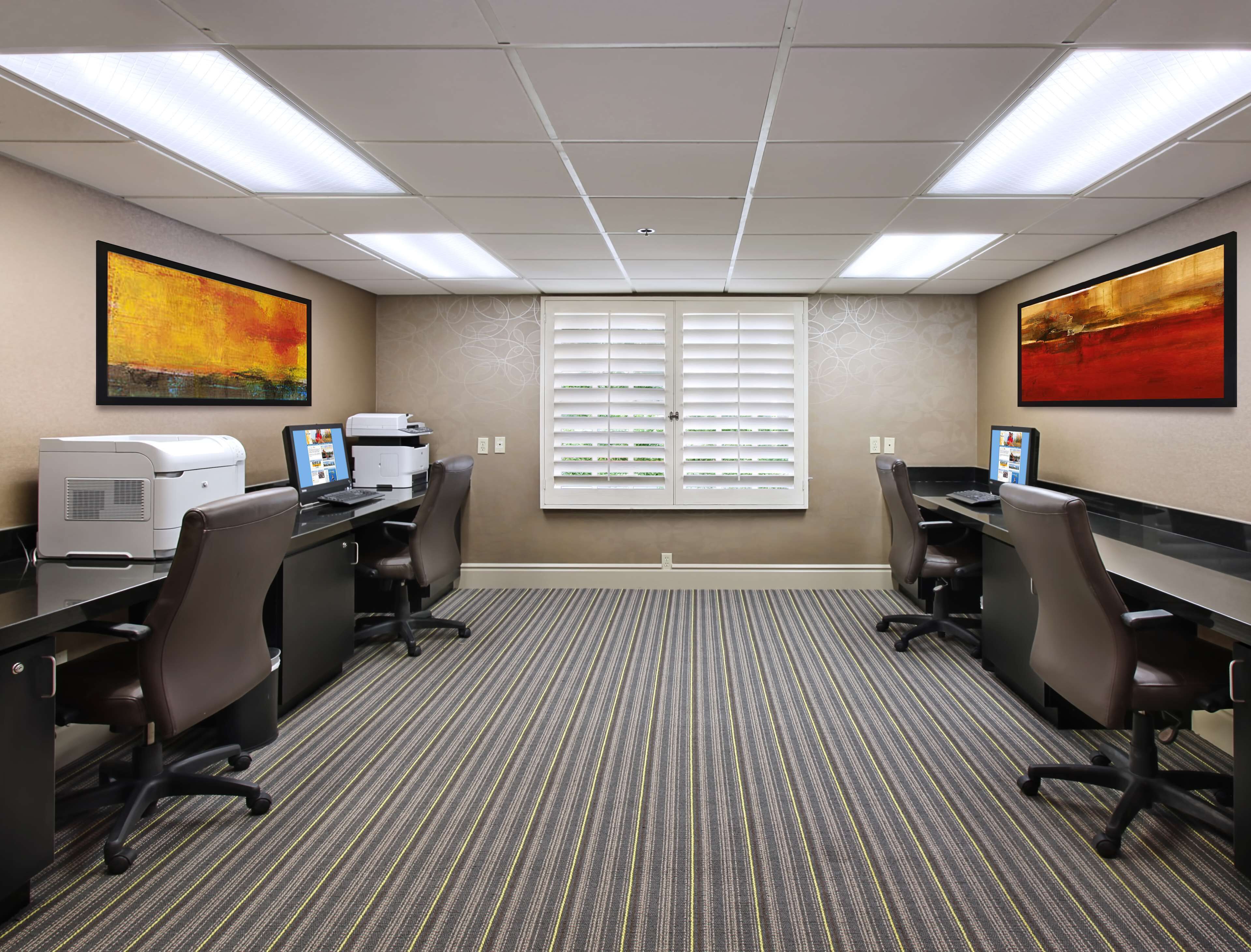 A conference room with two desks, chairs, a printer, and two large abstract paintings on the walls.