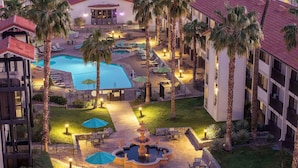 A resort with a swimming pool, palm trees, and outdoor seating areas.
