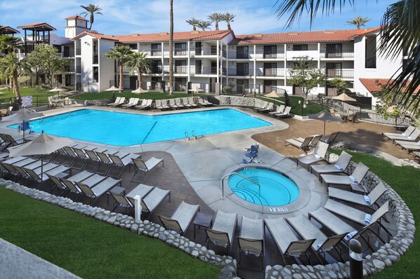 Un hotel con un amplio área de piscina, numerosas tumbonas y un jacuzzi circular.