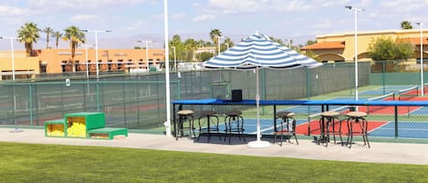 Una cancha de tenis con zona de estar, una red y una valla.