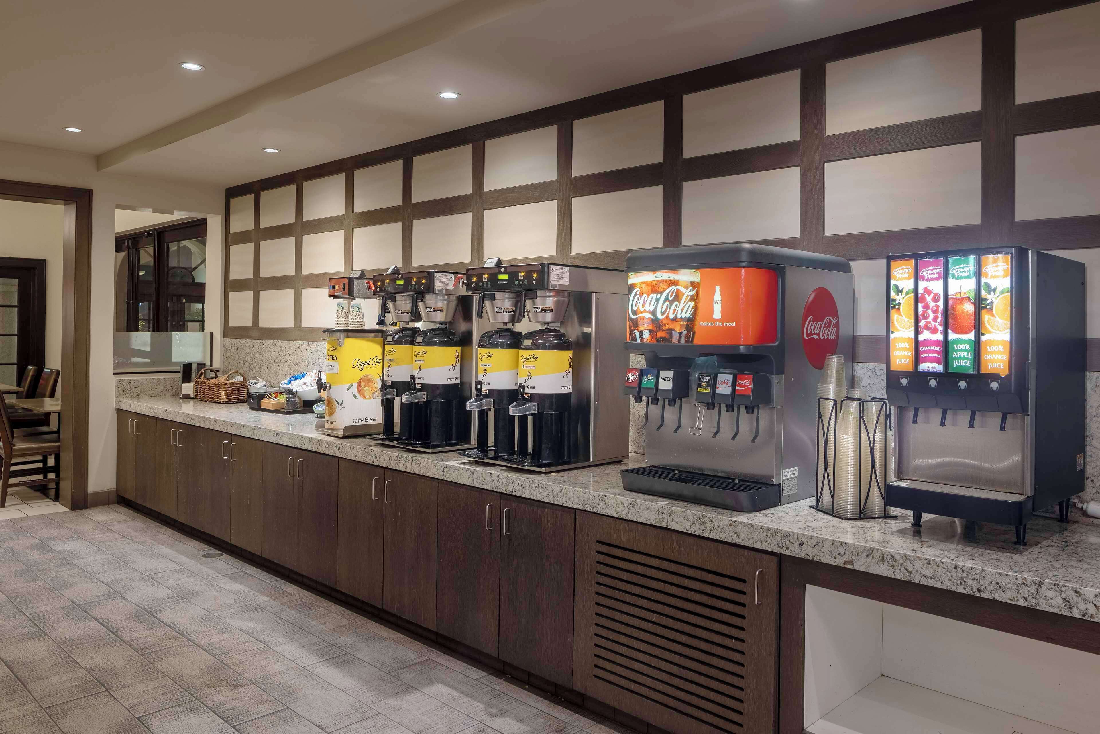 Una cocina de hotel con varias máquinas de café, un dispensador de Coca-Cola y un dispensador de zumo.