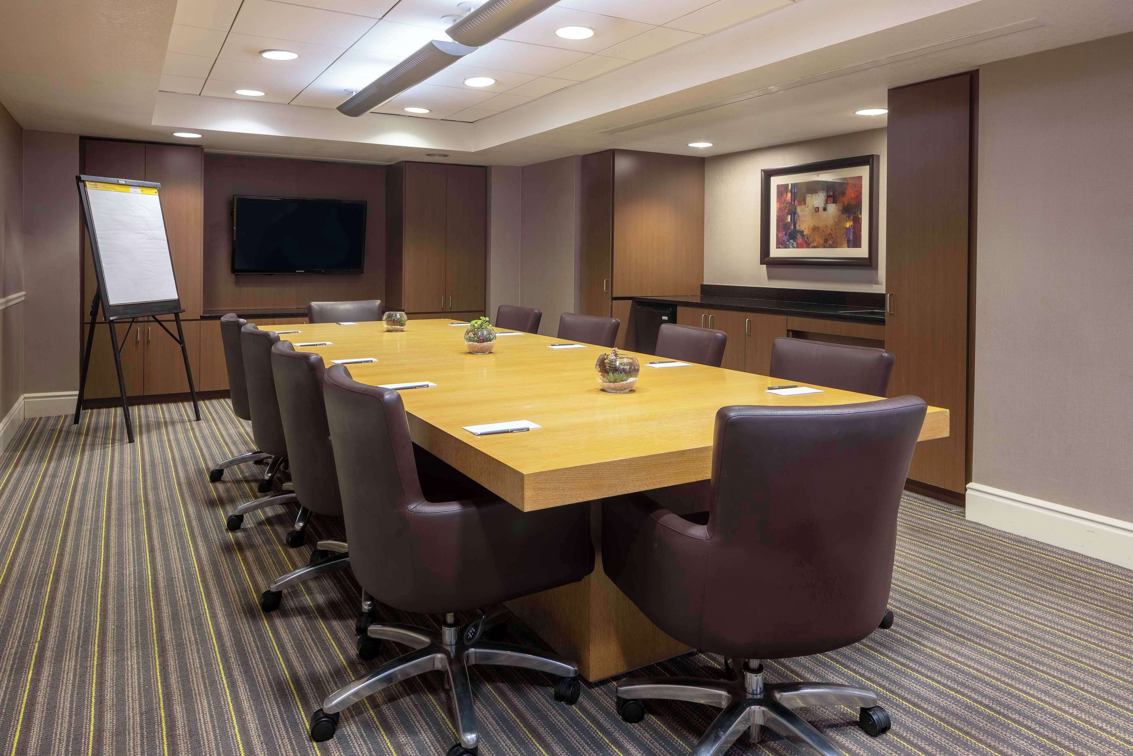 A conference room with a long table, chairs, a whiteboard, and a television on the wall.