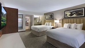 A hotel room with two beds, a TV, a bathroom, and a dining area.