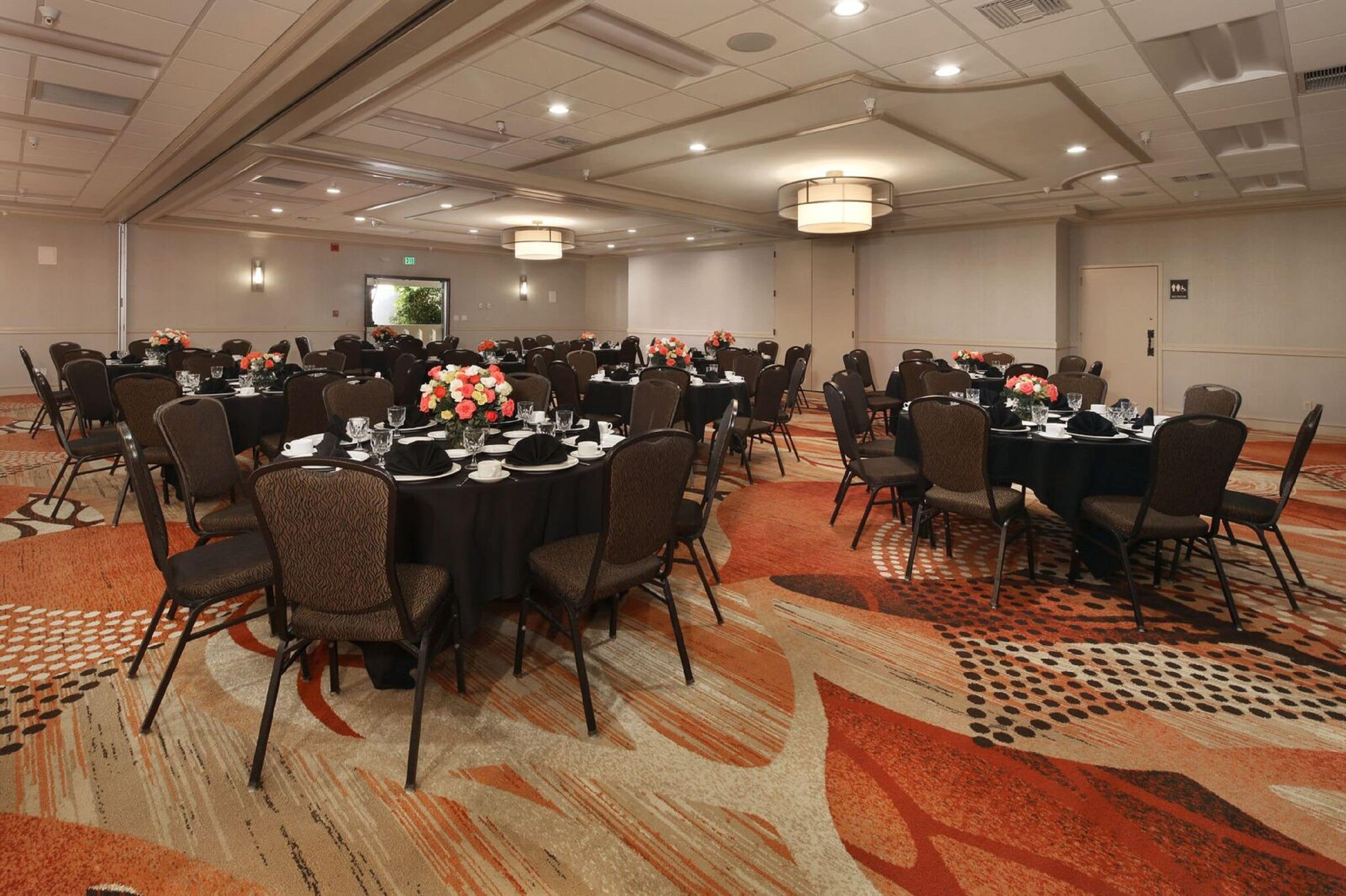 A conference room with multiple round tables, each set with chairs, plates, and floral centerpieces.