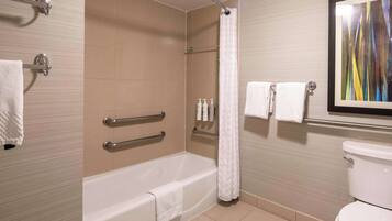 Un baño con bañera, ducha e inodoro. Se han instalado barras de apoyo en la bañera, una cortina de ducha y un perchero con toallas.