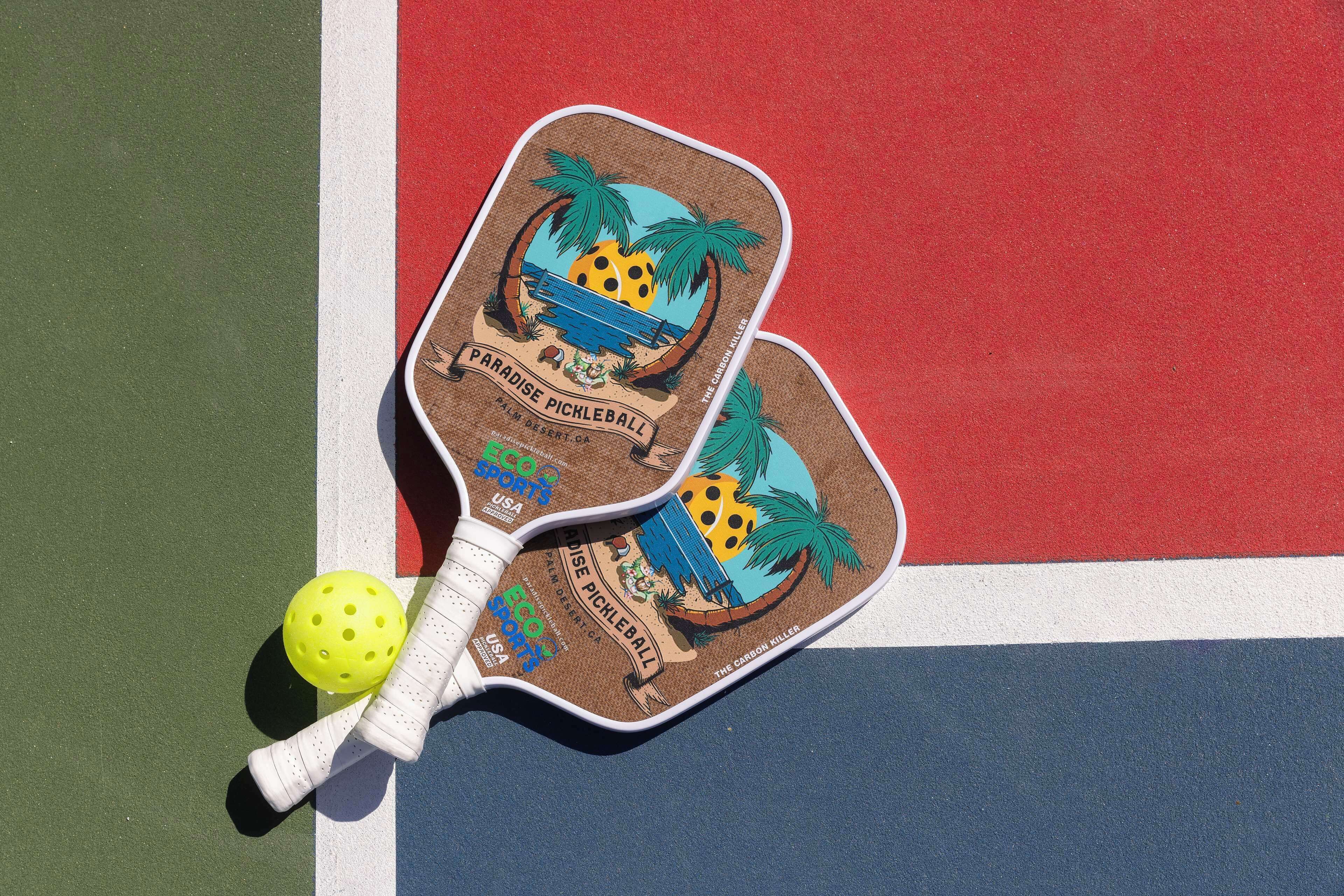 Two pickleball paddles with a tropical design on a court.