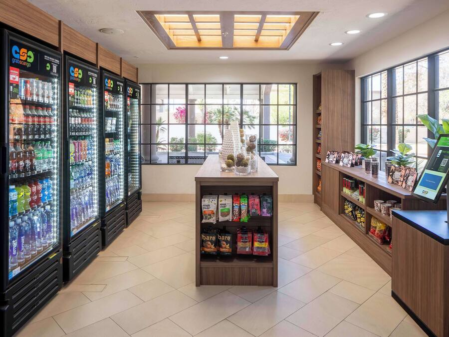 A vending area with multiple beverage dispensers, a central display case with snacks, and a reception desk with a digital kiosk.