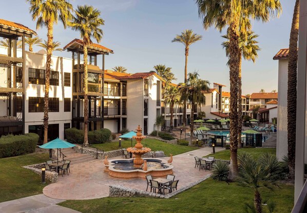 A courtyard with a fountain, outdoor seating, palm trees, and a pool area. - Embassy Suites by Hilton Palm Desert (Palm Desert)