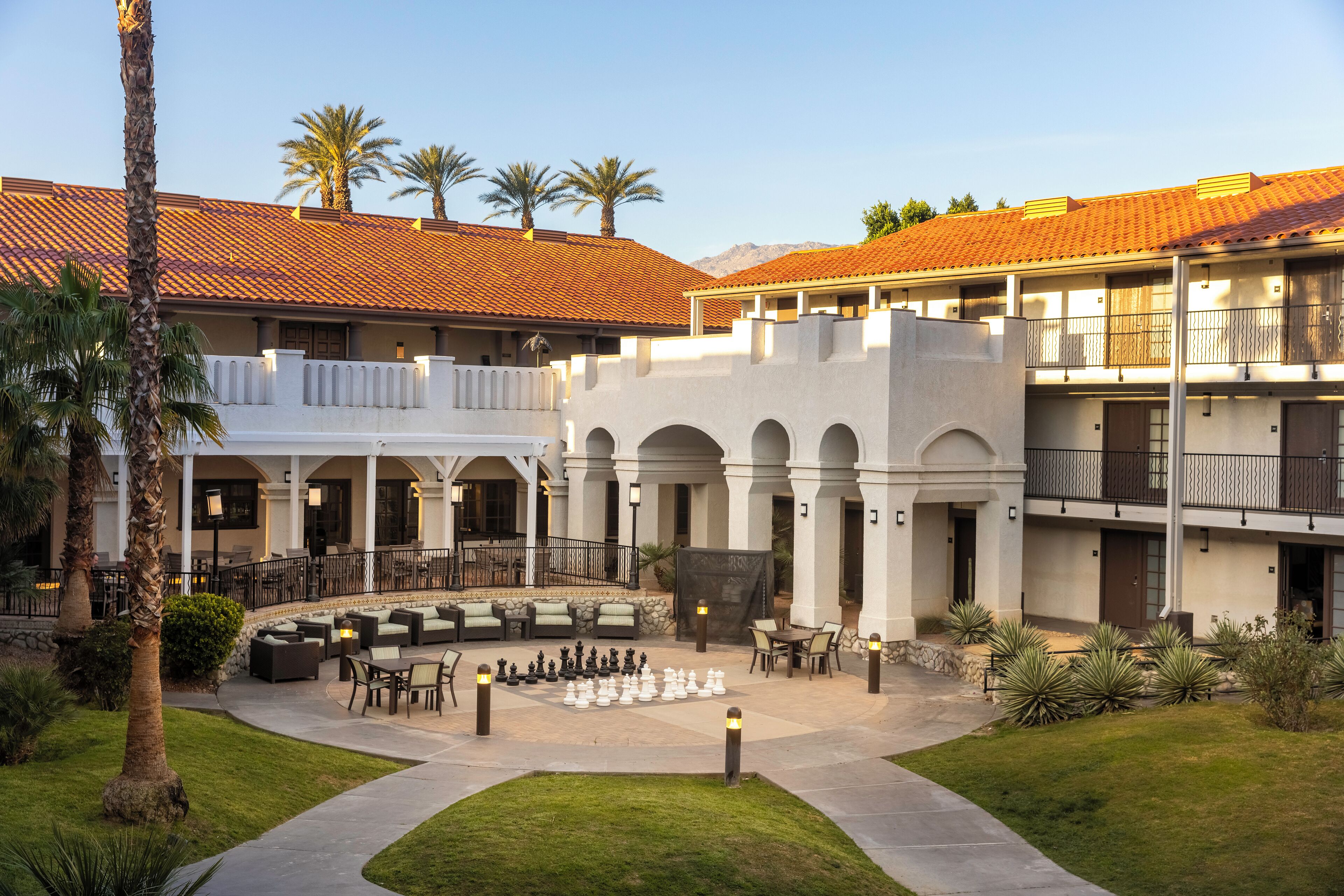 A courtyard with outdoor seating, palm trees, and a chessboard.