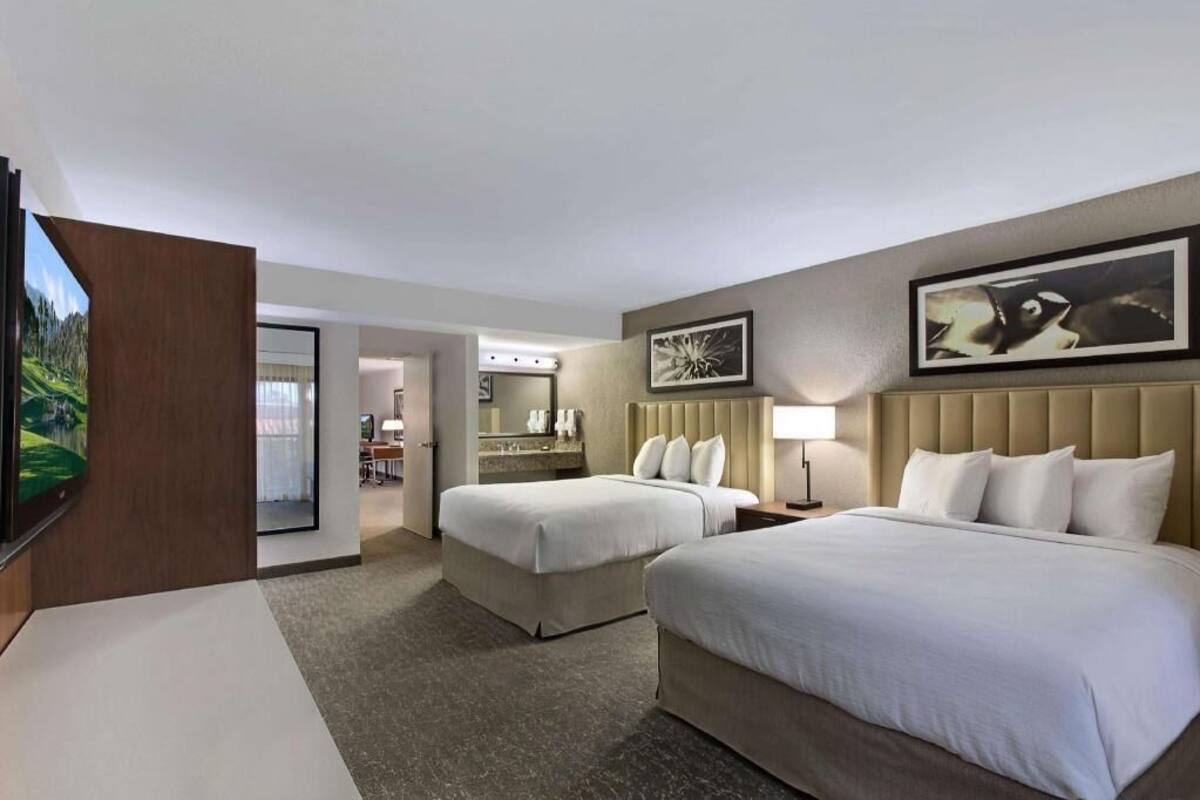 A hotel room with two beds, a TV, a bathroom, and a dining area.
