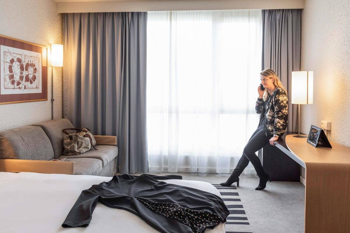 Une chambre d’hôtel avec un lit, un canapé, un bureau et une grande fenêtre avec des rideaux.