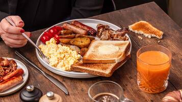 Een ontbijtbord met toast, eieren, bacon, worstjes en tomaten.