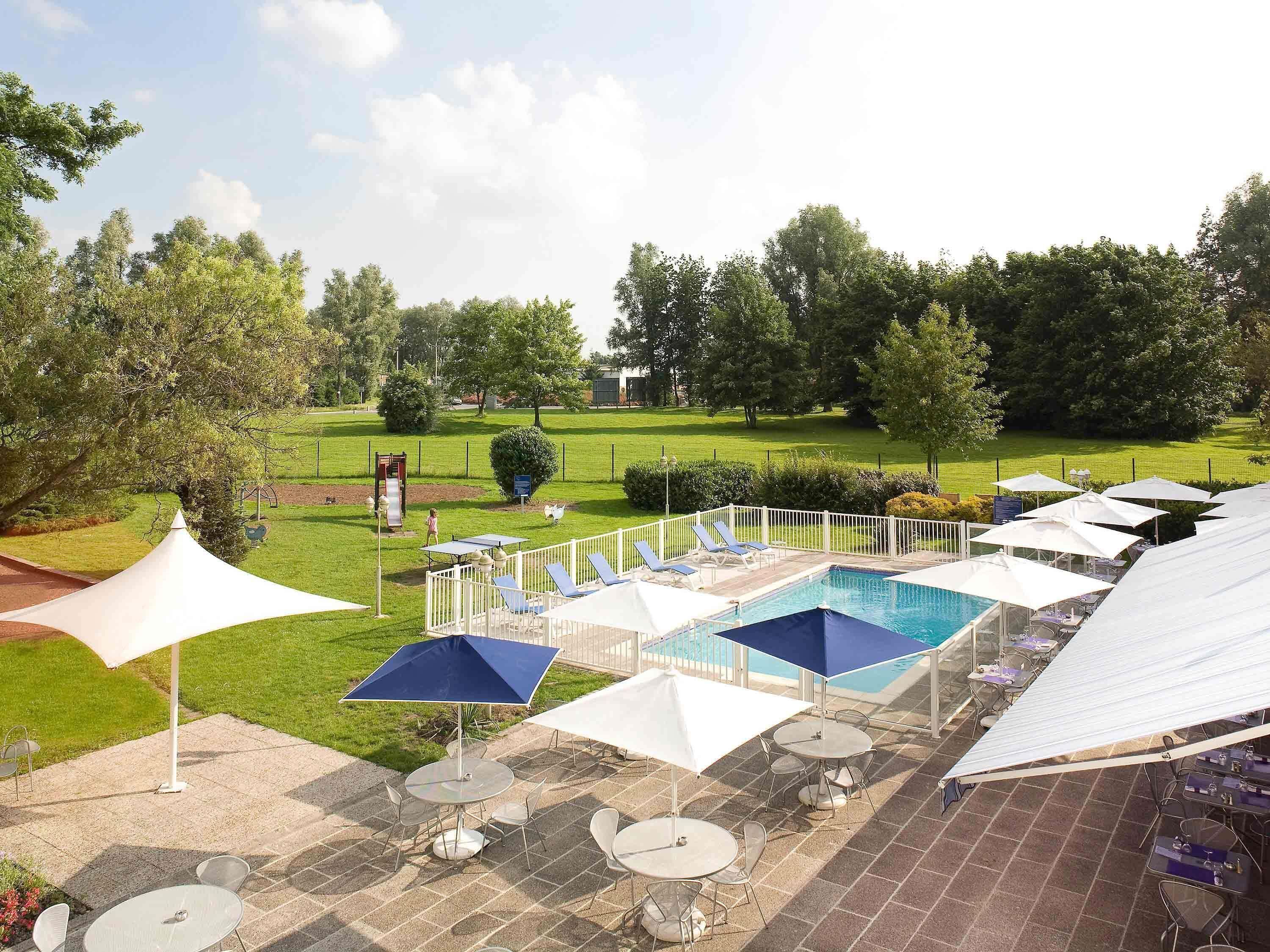 A pool area with lounge chairs and umbrellas, surrounded by a fenced garden.