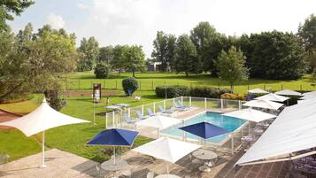 A pool area with lounge chairs and umbrellas, surrounded by a fenced garden.