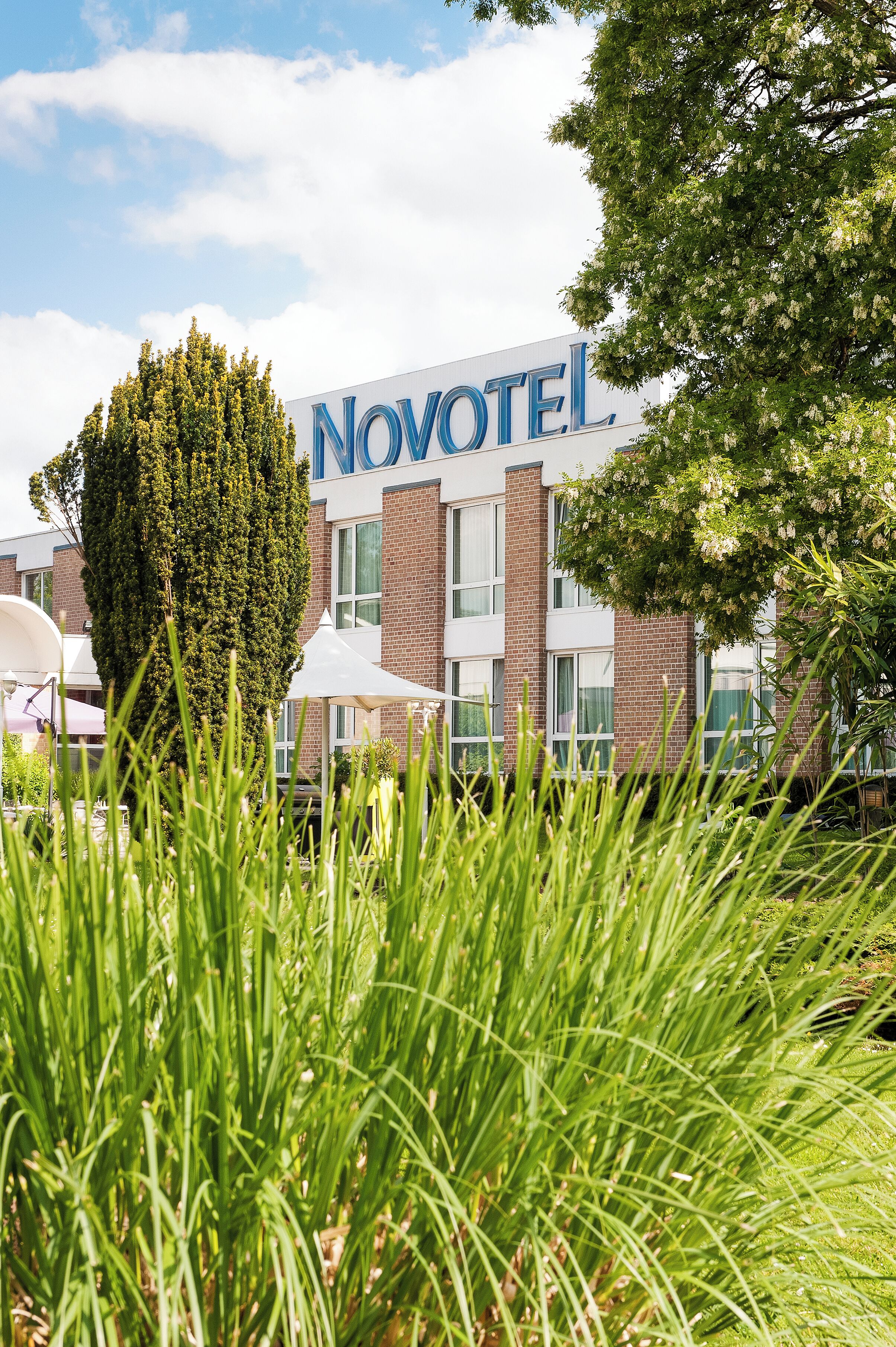 A Novotel hotel with a prominent sign, surrounded by greenery and outdoor seating areas.