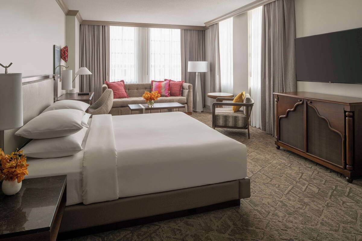 A hotel room with a large bed, a sofa, a small table, a chair, a TV, and a cabinet.