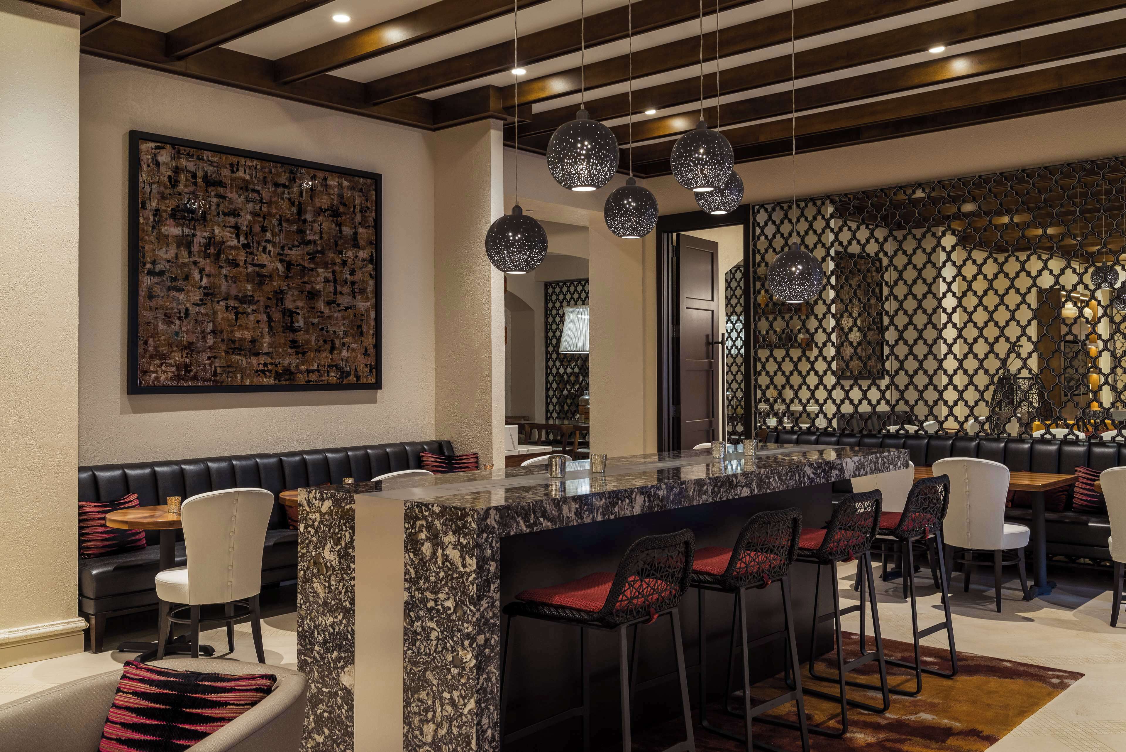 Zona de bar moderna con encimera de mármol, taburetes negros y blancos e iluminación colgante.