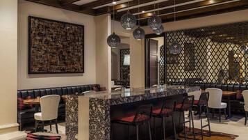 Zona de bar moderna con encimera de mármol, taburetes negros y blancos e iluminación colgante.