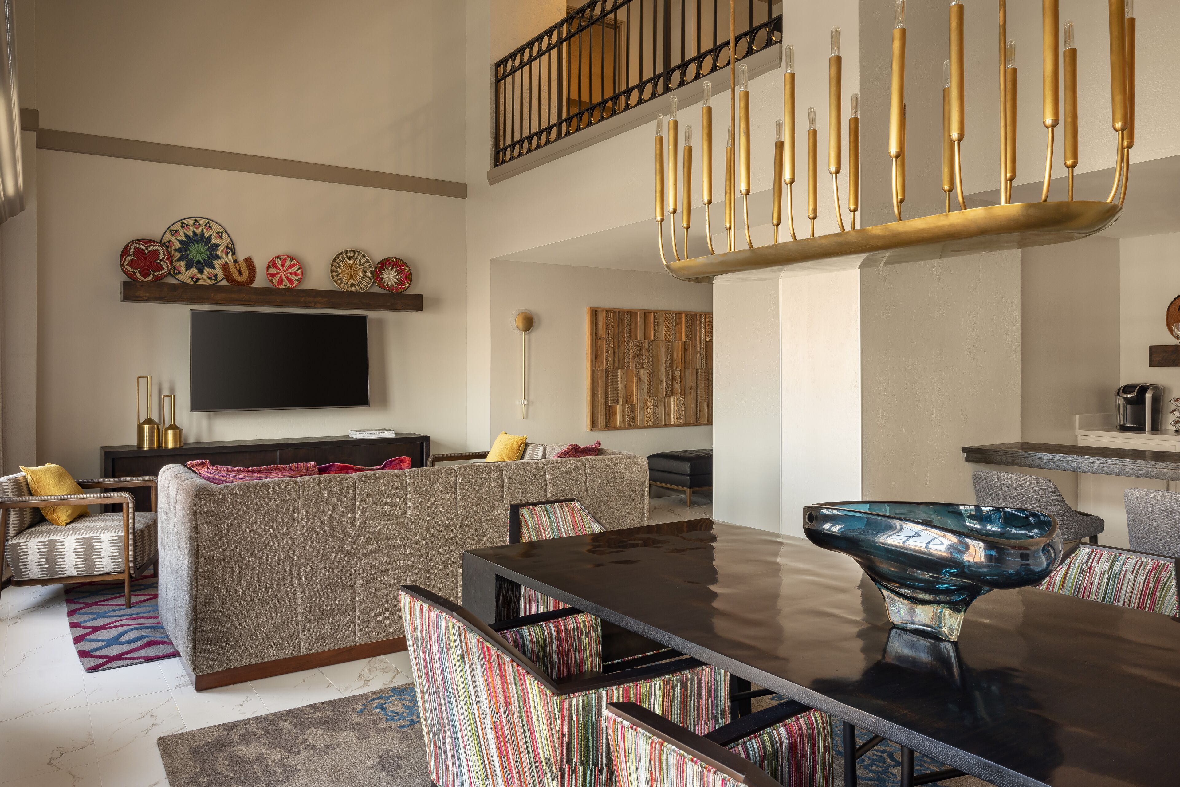 Una sala de estar moderna con un televisor de pantalla plana grande, una mesa de comedor con sillas, una escalera con barandilla y decoración en la pared.