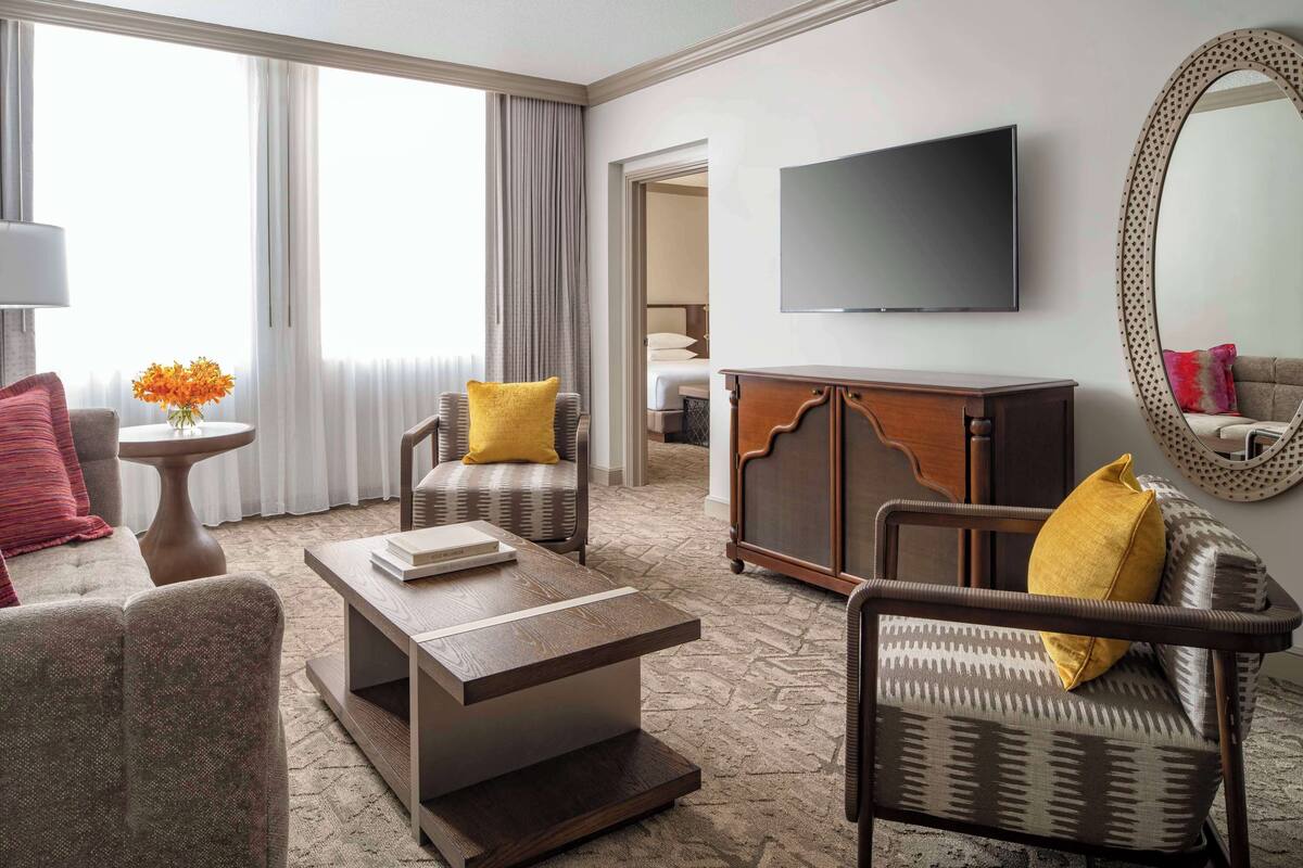 A hotel room with a sofa, armchair, coffee table, TV, and a large mirror.