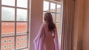 A room with large windows, a patterned carpet, and a view of buildings outside.