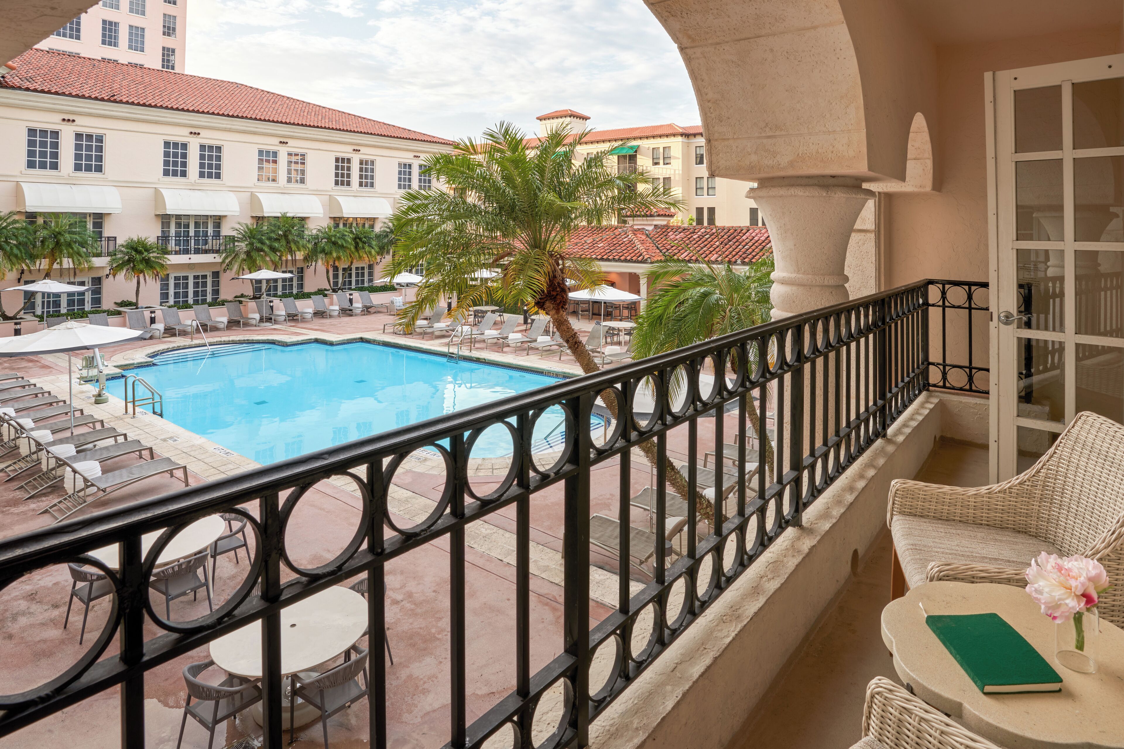 Ein Balkon mit Blick auf einen Pool, Liegestühle und eine Palme.