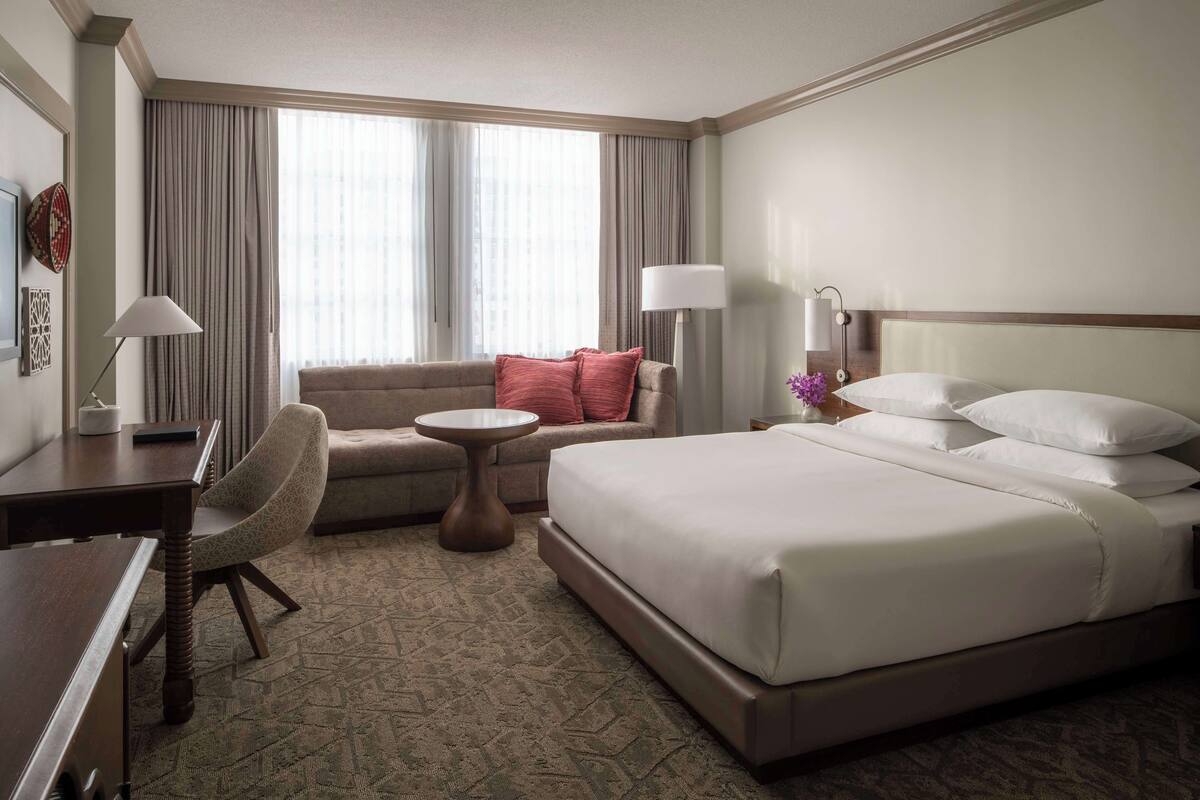 A hotel room with a bed, a desk, a chair, a small table, and a sofa.