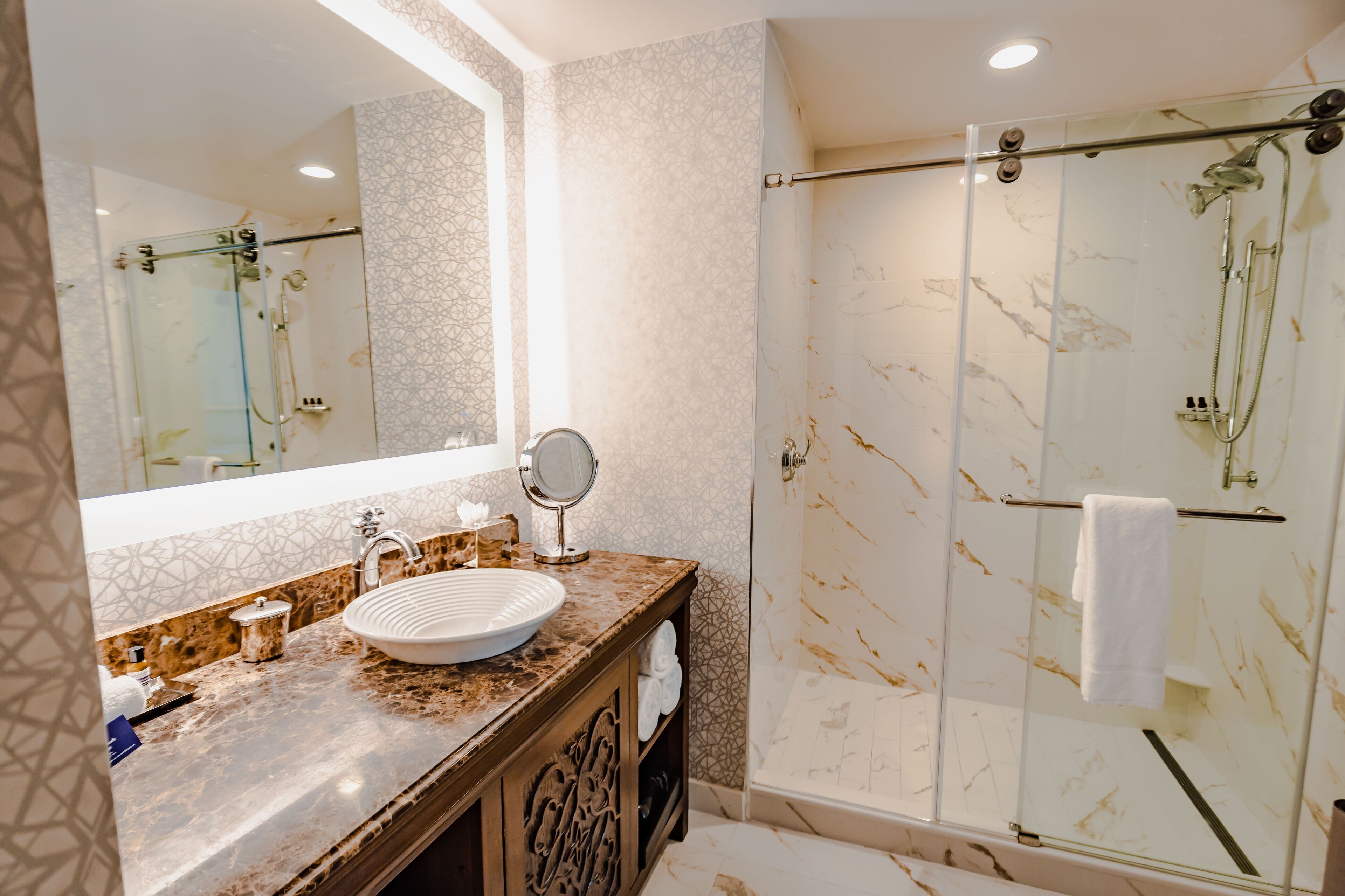 A bathroom with a marble sink, a large mirror, a glass-enclosed shower, and a towel rack.