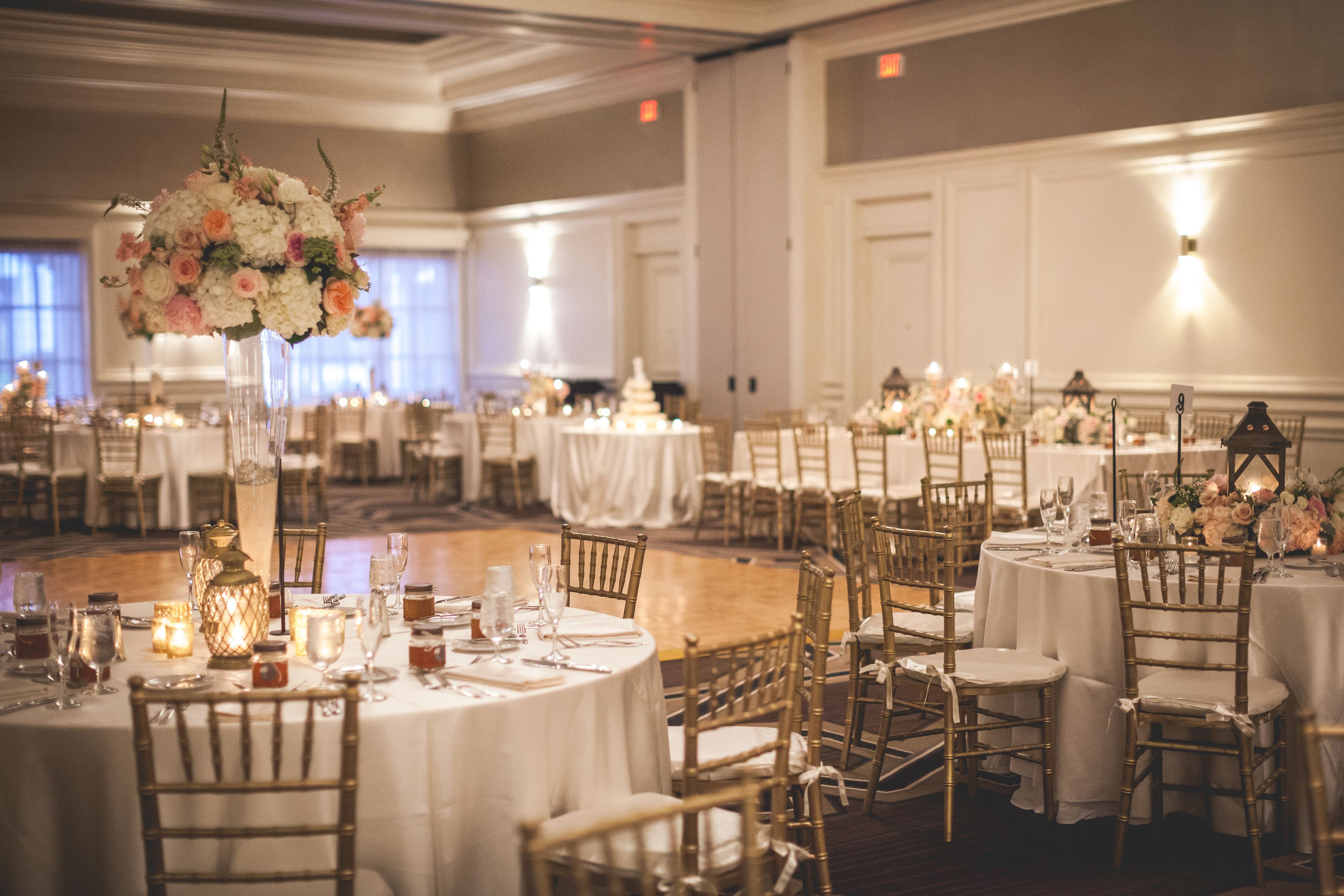 Une salle de banquet avec des tables rondes, des chaises dorées et des centres de table floraux.