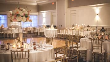 Une salle de banquet avec des tables rondes, des chaises dorées et des centres de table floraux.
