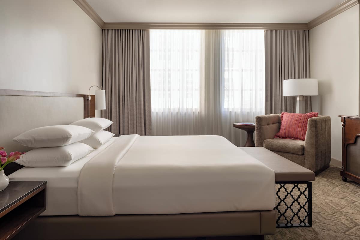 A hotel room with a bed, a chair, a nightstand, and a lamp.