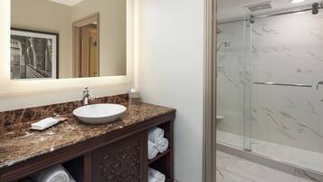A bathroom with a marble countertop, a sink, a glass shower enclosure, and a mirror with a framed picture.
