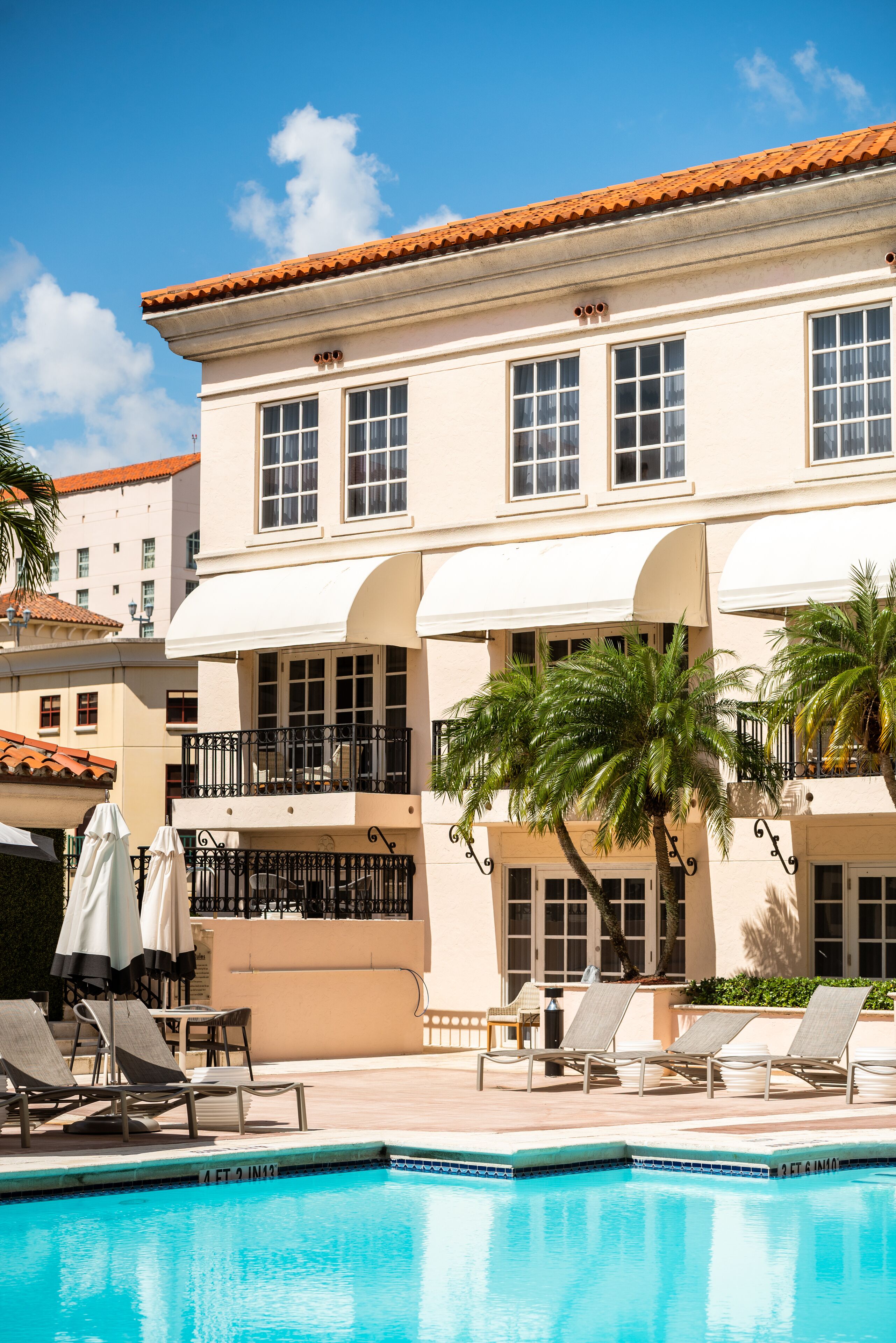 A hotel with a swimming pool, lounge chairs, and palm trees.