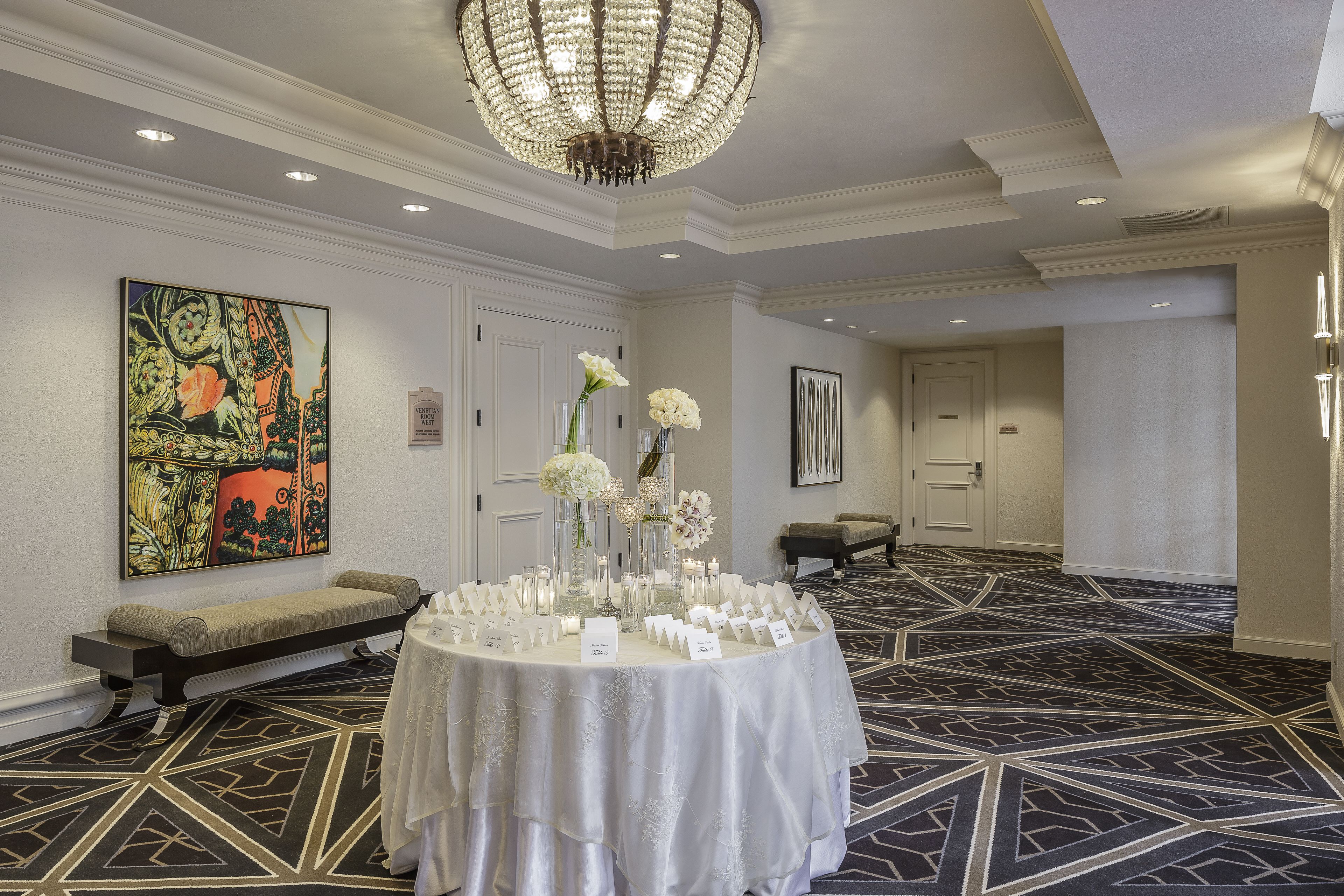 Une salle de conférence avec une table ronde, des compositions florales blanches, un banc et un grand tableau abstrait accroché au mur.