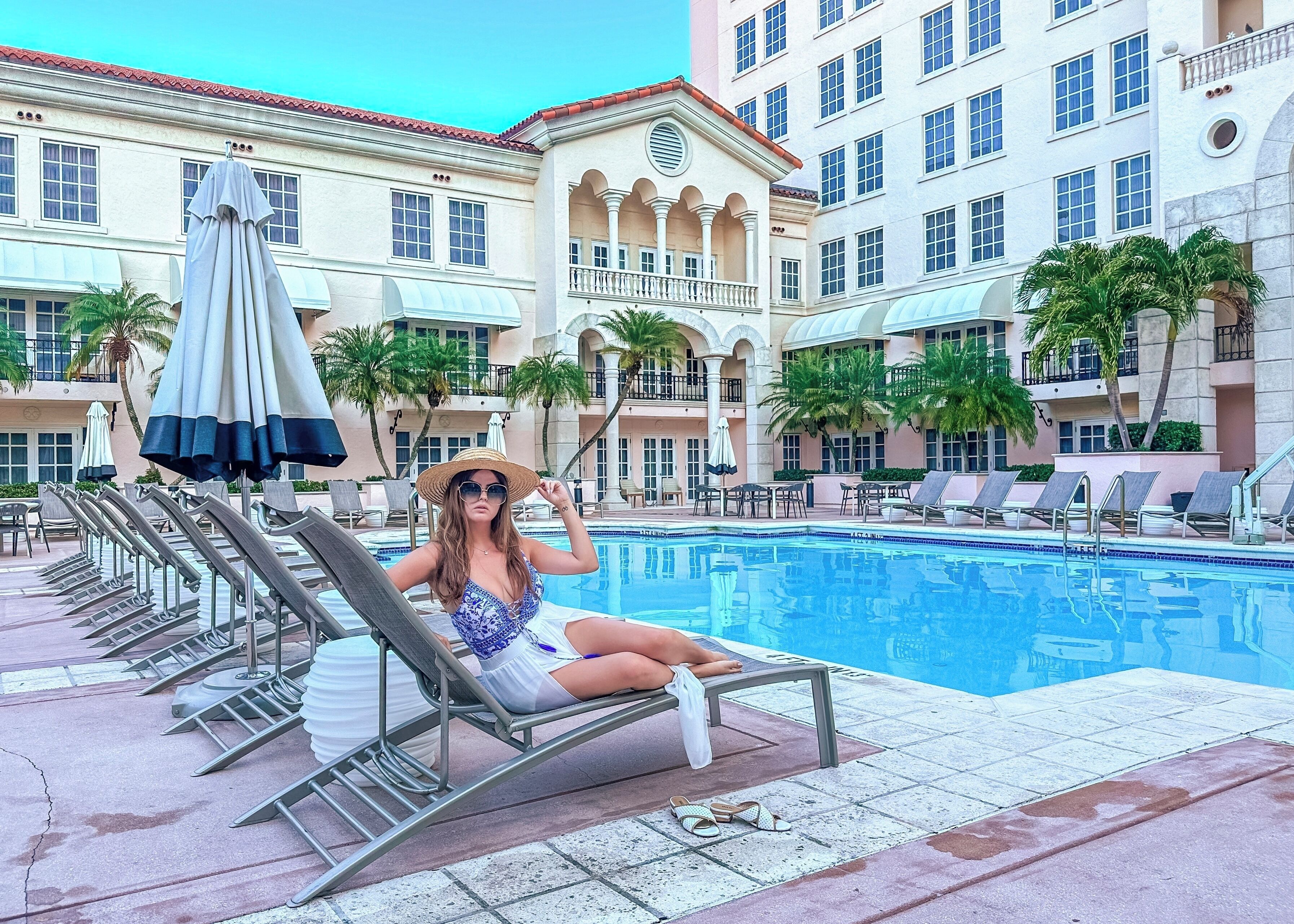 A poolside area with lounge chairs, a pool, and a building with balconies and windows.