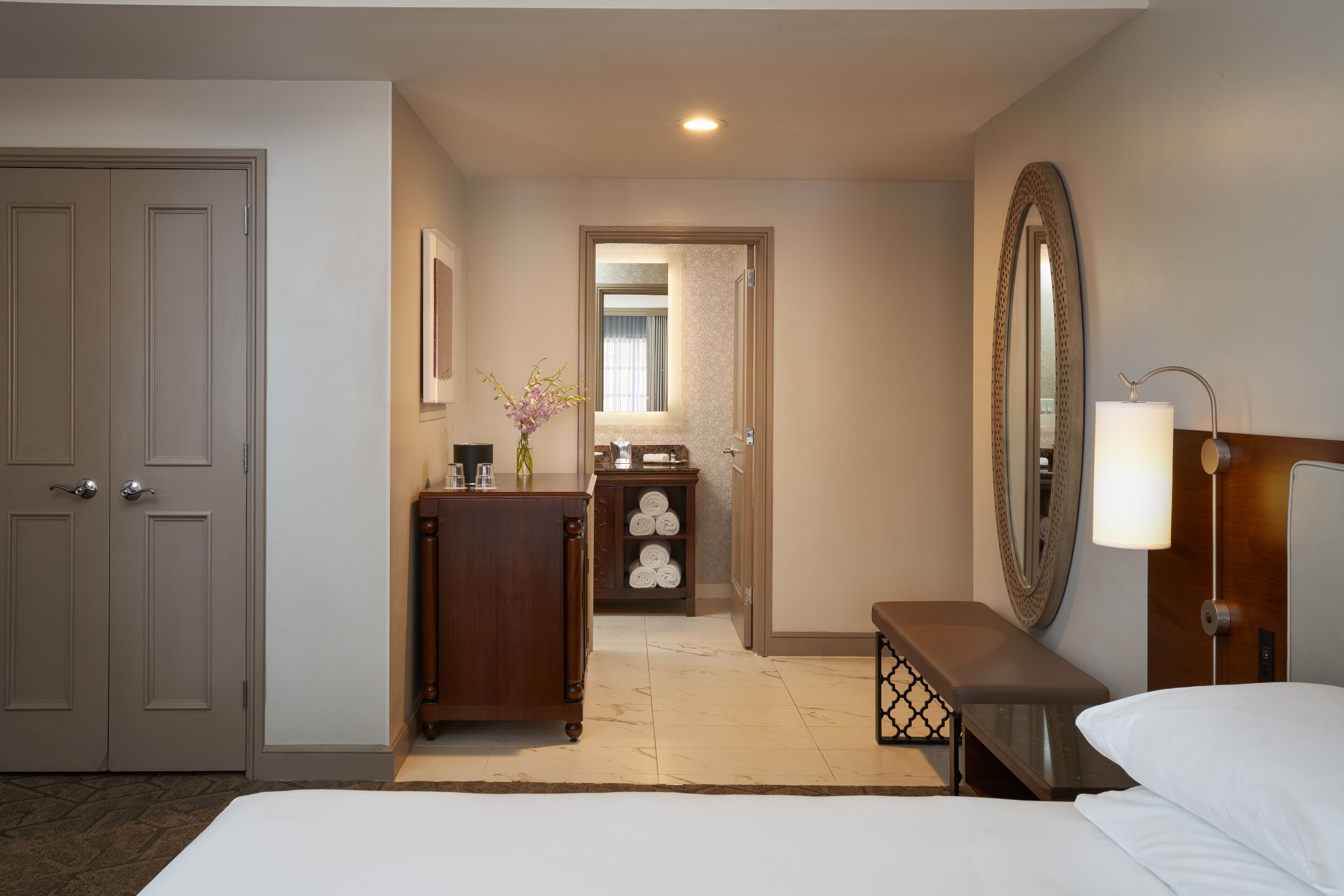A hotel room with a bed, a desk, a dresser, a mirror, and a bathroom visible through an open door.