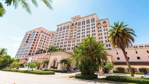 Un grand hôtel à étages, avec une cour intérieure agrémentée de palmiers et un ciel d’un bleu éclatant.