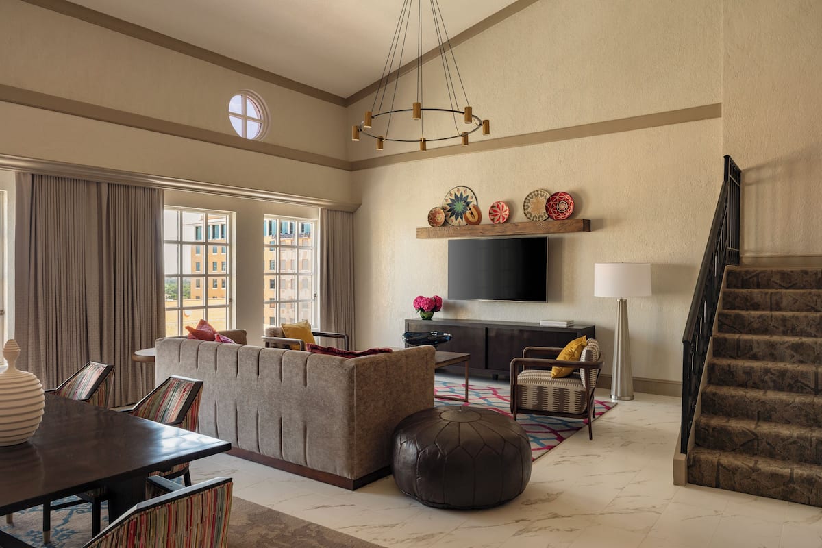 A spacious living room with a large window, a sofa, a dining table, and a staircase.