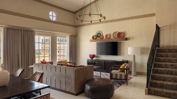 A spacious living room with a large window, a sofa, a dining table, and a staircase.
