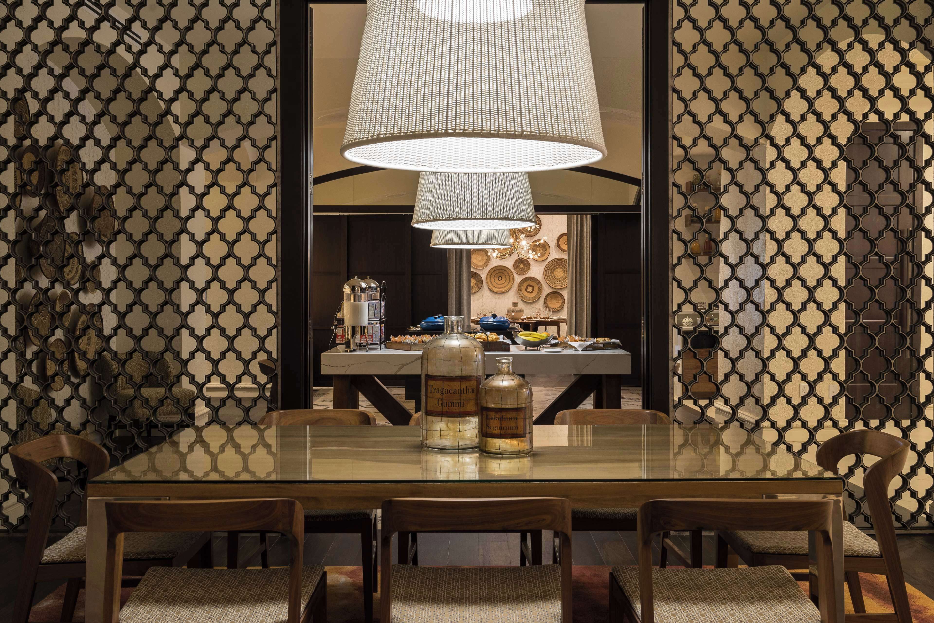 A dining area with a glass table, wooden chairs, and a large hanging light fixture.